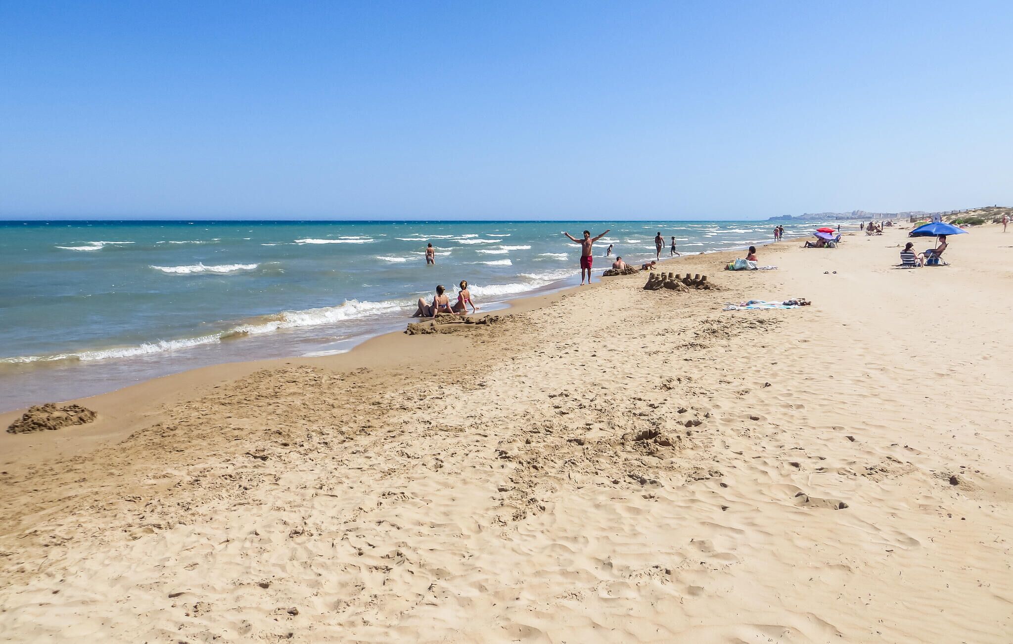 A sandy beach with footprints and a few people.