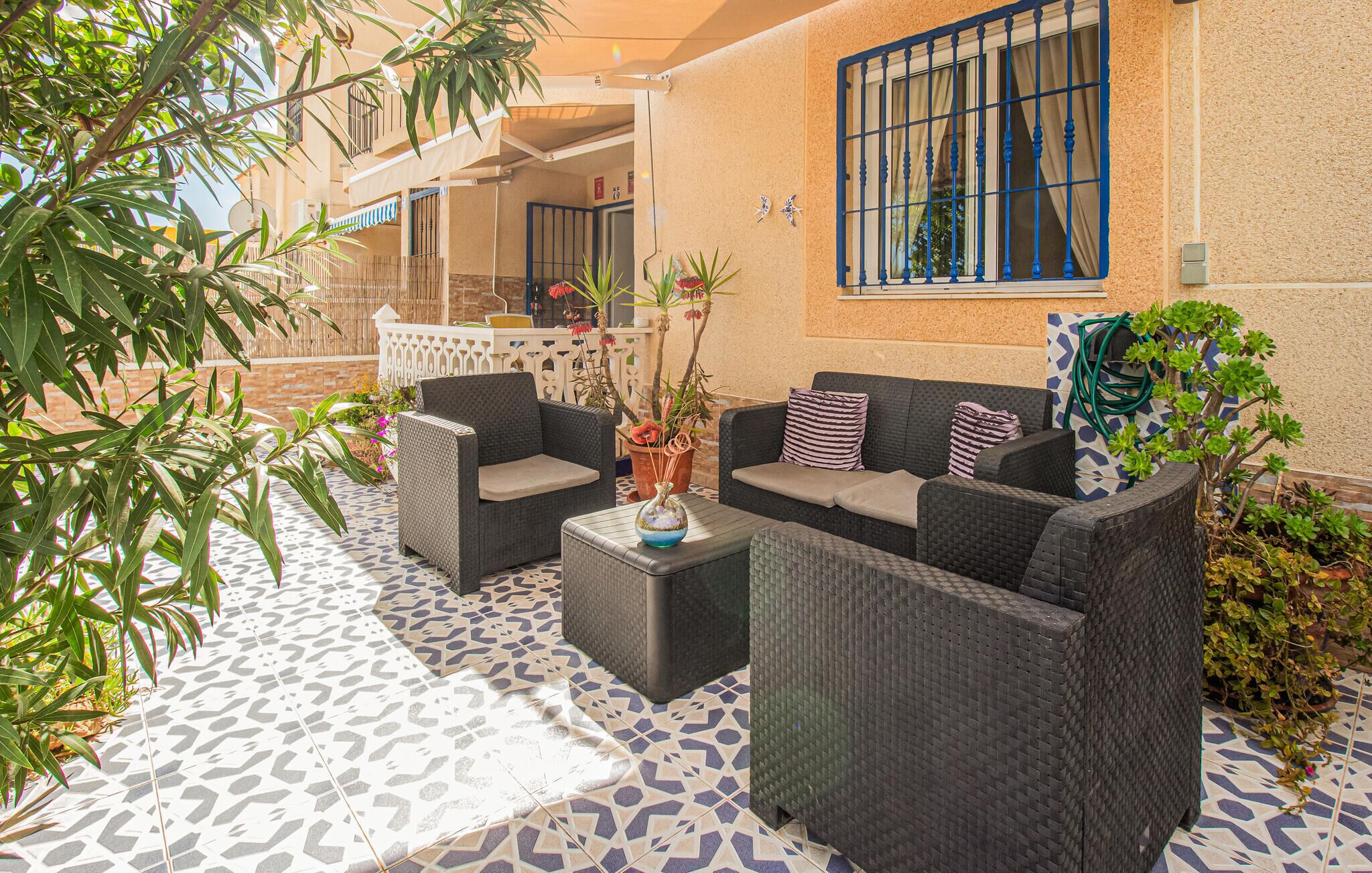 A patio area with wicker furniture, a patterned floor, and potted plants.