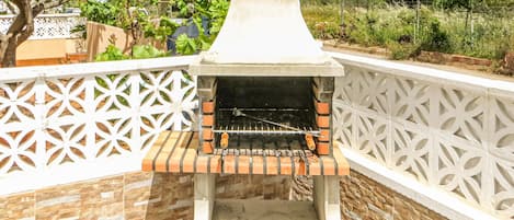 Una parrilla de ladrillo para barbacoa al aire libre con chimenea, rodeada por una valla decorativa blanca.