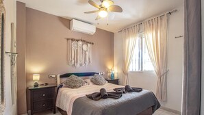 A bedroom with a bed, bedside tables, a ceiling fan, a wall-mounted air conditioner, and a window with curtains. - Stunning apartment in Torrevieja (Torrevieja)