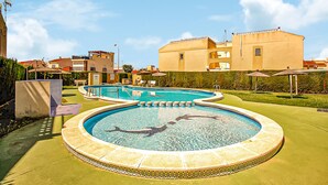 A swimming pool with a circular design, surrounded by a tiled deck. There are lounge chairs and umbrellas in the background, and a building with balconies is visible. - Stunning apartment in Torrevieja (Torrevieja)