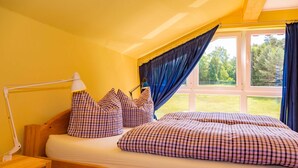 A bedroom with a bed, a nightstand, a lamp, and a window with curtains. - Apartment 5 - Usedom Landhaus Morgenitz (Mellenthin OT Morgenitz)