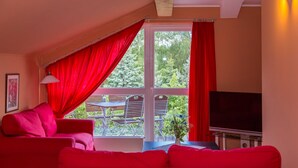 A room with a red sofa, a dining table with chairs, a TV, and a window with red curtains. - Apartment 5 - Usedom Landhaus Morgenitz (Mellenthin OT Morgenitz)