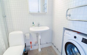 Casa de banho com sanita, lavatório e máquina de lavar roupa.