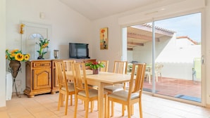 Een eethoek met een tafel, stoelen, een televisie en een schuifdeur naar een terras.