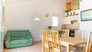 Een compacte keuken met een eethoek, met een groene bank, houten stoelen, een betegelde vloer en een witte deur.