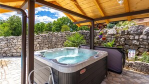 Boblebad under et træbeklædt pergola med en stenvæg og plantekasser i baggrunden.
