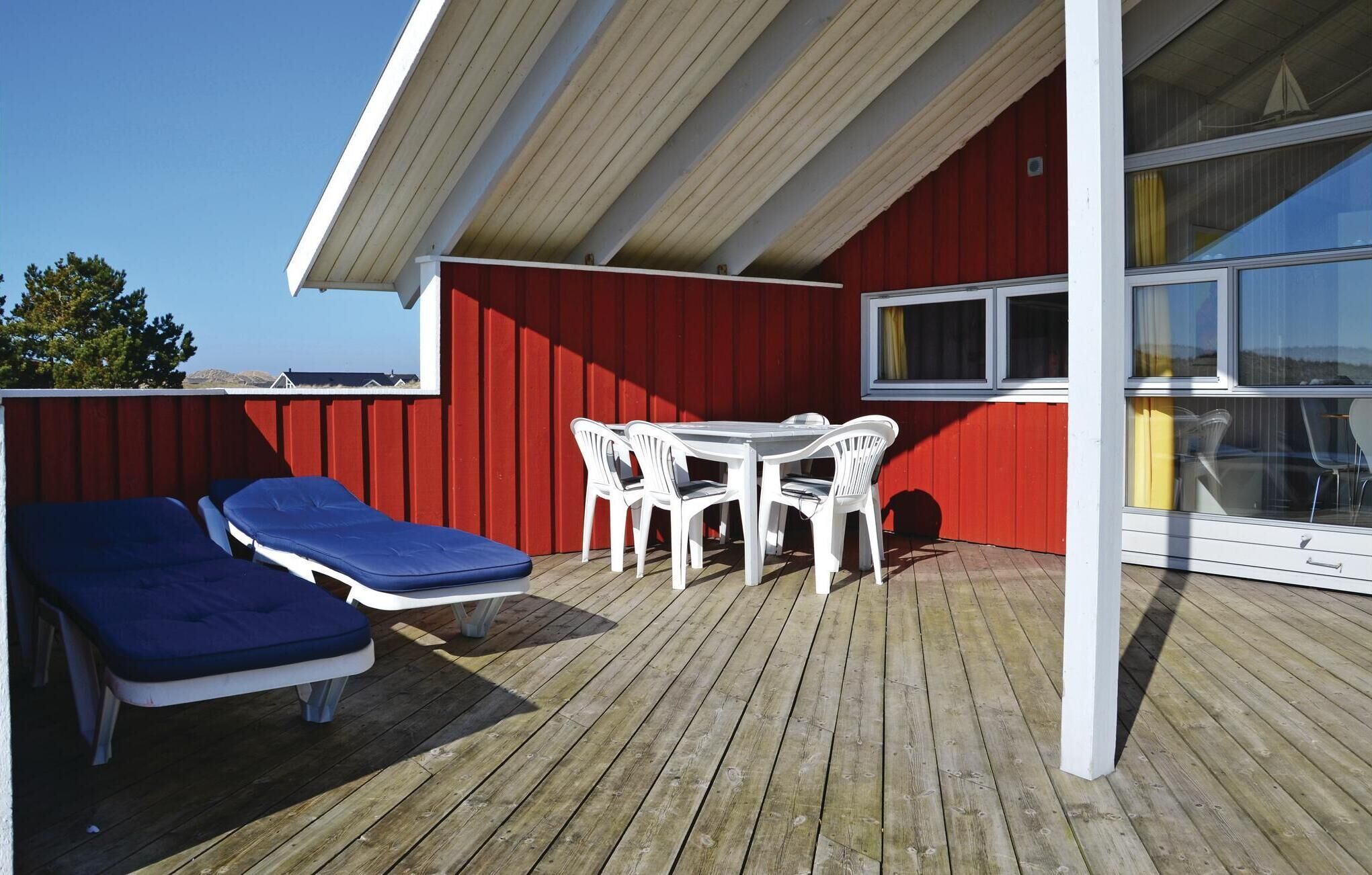 A wooden deck with a red wall, a table with chairs, and a blue lounge chair.
