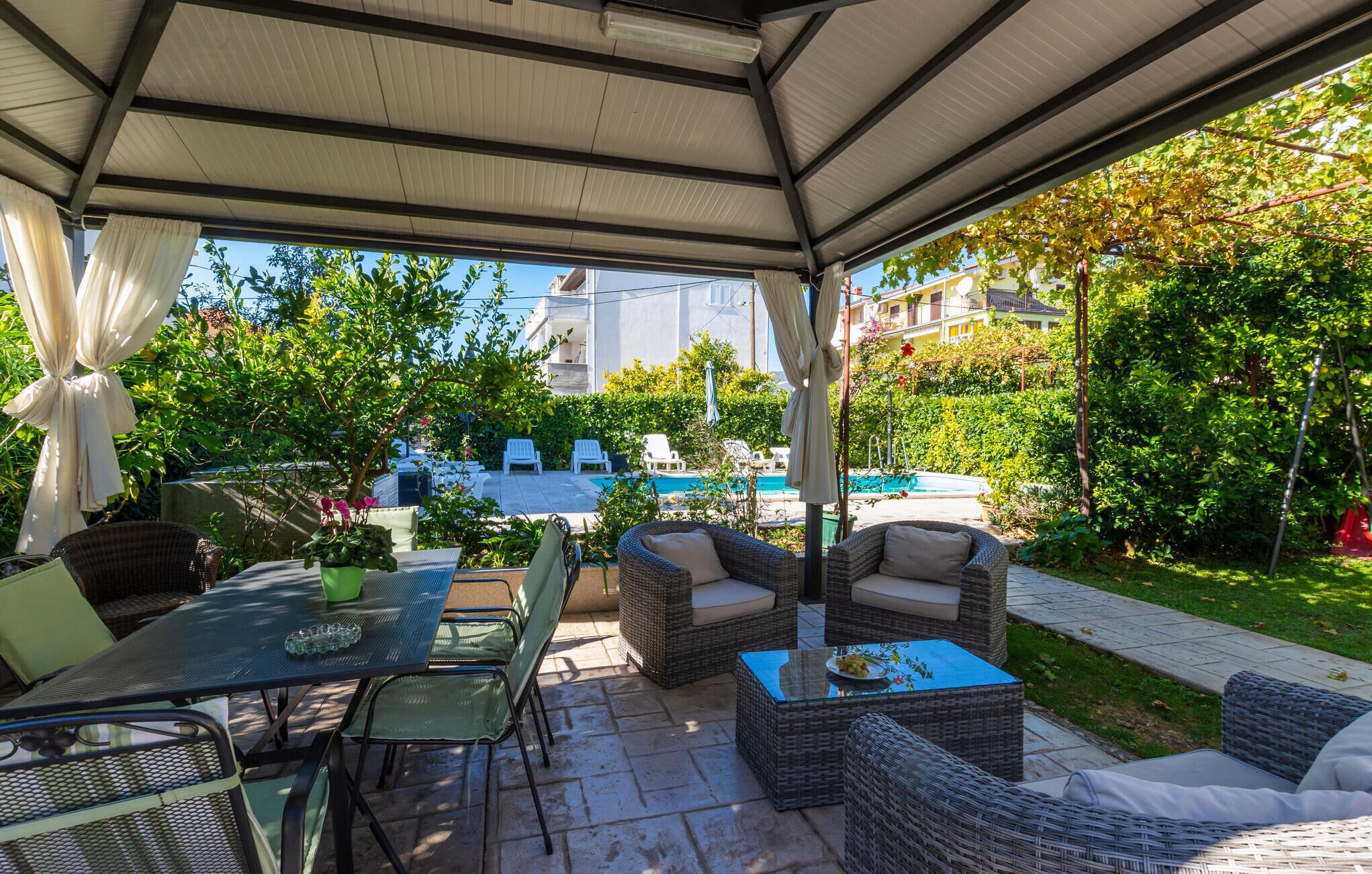 Eine Terrasse im Freien mit Korbmöbeln, einem Glastisch und einem Pool im Hintergrund.