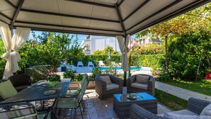 Eine Terrasse im Freien mit Korbmöbeln, einem Glastisch und einem Pool im Hintergrund.