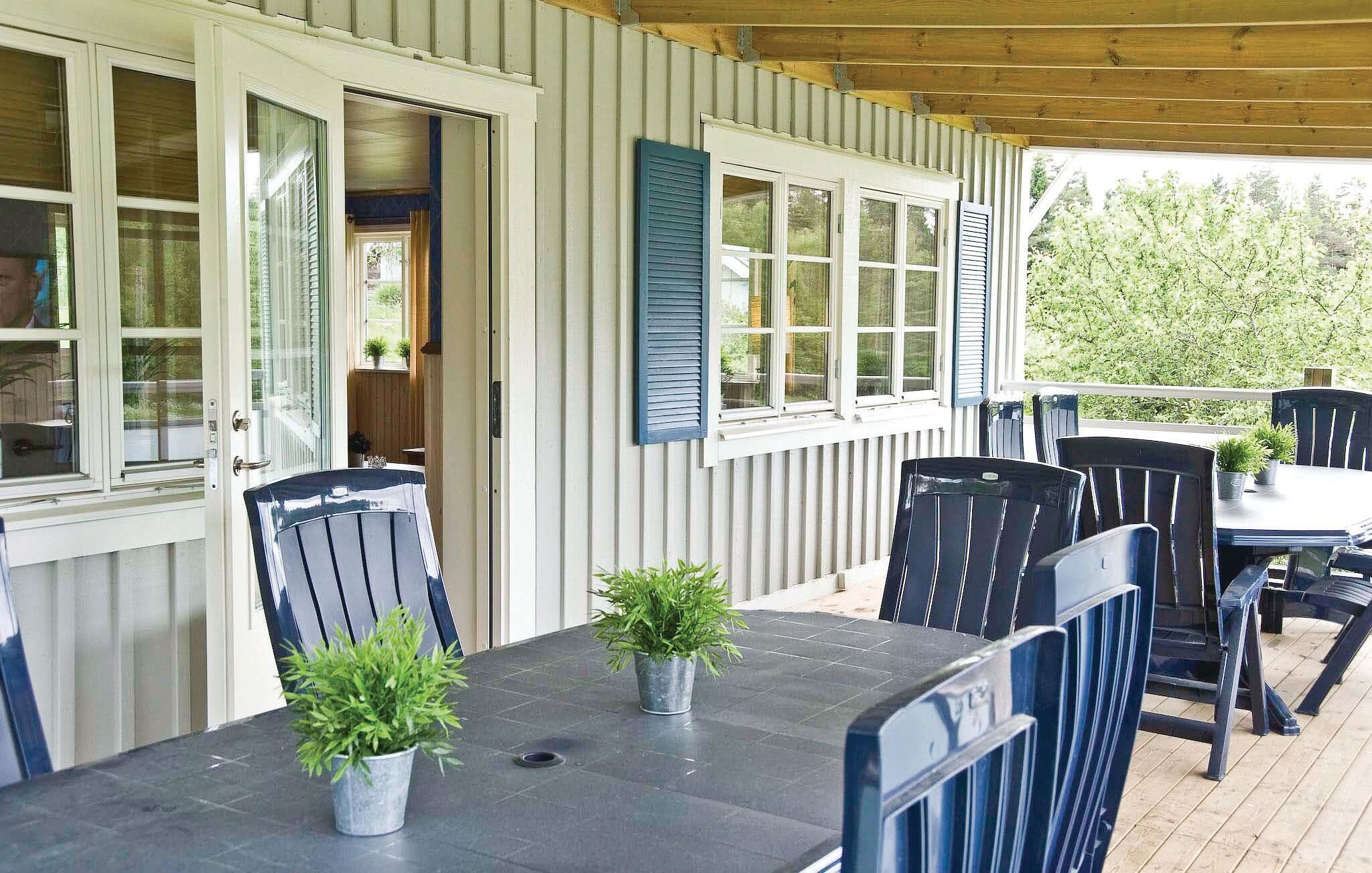 A covered outdoor patio with a table and chairs, potted plants, and a view of greenery.