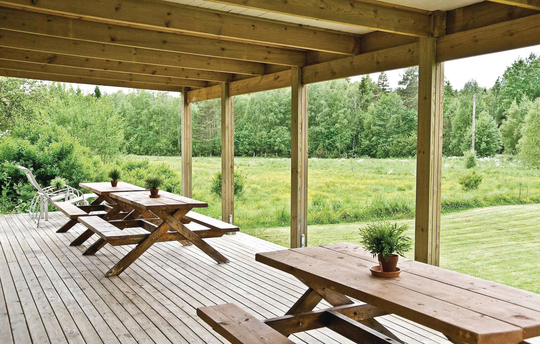 Eine Holzterrasse im Freien mit Picknicktischen und Kübelpflanzen, umgeben von einer üppigen Grünlandschaft.
