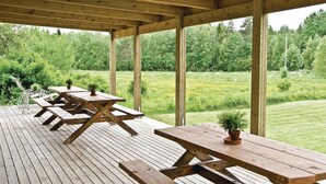 Eine Holzterrasse im Freien mit Picknicktischen und Kübelpflanzen, umgeben von einer üppigen Grünlandschaft.
