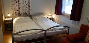 Ein Doppelbett mit zwei Nachttischen, jeweils mit einer Lampe, ein Fenster mit Vorhängen und ein roter Sessel.