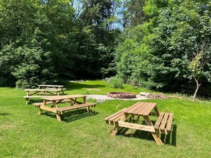 Un espace pique-nique équipé de tables et de bancs en bois, entouré d’une végétation luxuriante et d’arbres.