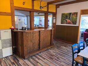 A wooden bar area with a patterned floor, a dining area with blue chairs, and a painting on the wall.