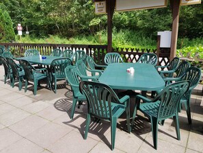 Tables et chaises pour les repas en plein air, entourées d’une clôture en bois, avec de la verdure en arrière-plan.