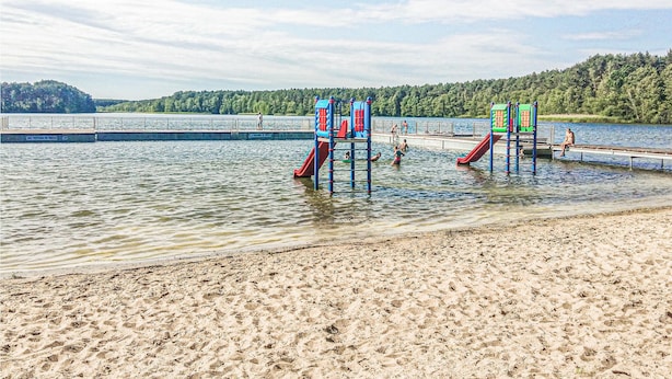 Ein Strand mit einer Spielplatzkonstruktion und einer Brücke über dem Wasser.