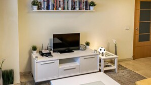 Un salon avec un meuble de rangement blanc pour l’équipement audiovisuel, un téléviseur à écran plat, une table basse et une bibliothèque remplie de livres.