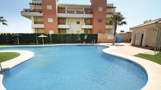 Une piscine à bord incurvé, entourée d’une haie basse et, au fond, un bâtiment doté de balcons.