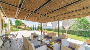 Eine Terrasse im Freien mit Korbmöbeln und Steinboden, mit Blick auf einen angelegten Garten und ferne Hügel.