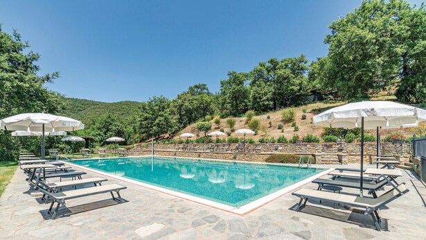 Ein rechteckiger Pool mit Liegestühlen und Sonnenschirmen auf einer Steinterrasse, umgeben von Grünflächen und Hügeln.