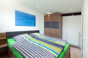 A modern bedroom with a bed, a large window, and a white brick wall.