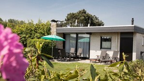 Una casa moderna con un patio, que incluye una mesa, sillas y un paraguas verde.