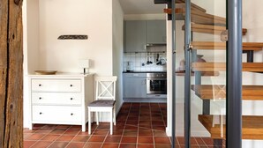 Een moderne keuken met een inbouwoven, een eethoek met een witte tafel en stoel, en een houten trap.