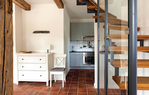 A modern kitchen with a built-in oven, a dining area with a white table and chair, and a wooden staircase.