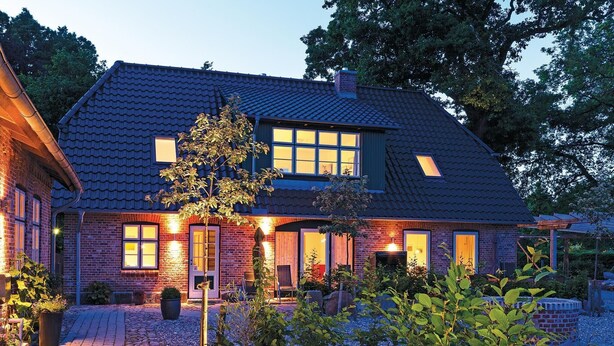 Een tweelaags huis met een donker betegeld dak, bakstenen muren en meerdere ramen.