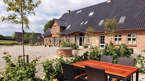 Een stenen huis met schuin dak, een grindpad en tuinmeubilair.