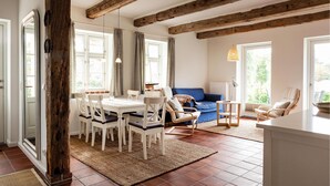 Een eetgedeelte met een houten tafel en stoelen, een blauwe bank en uitzicht op het landschap door grote ramen.