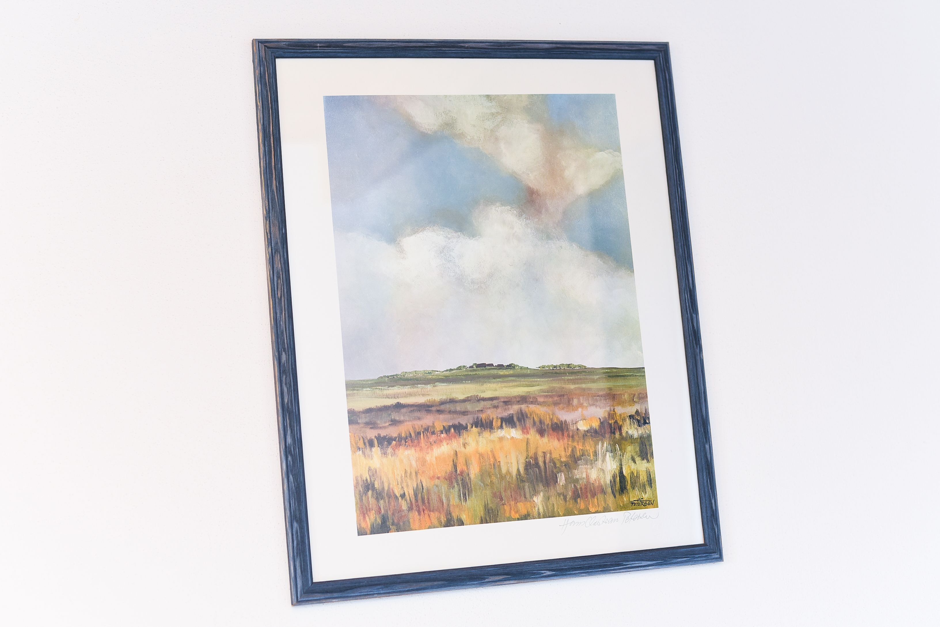 A framed landscape painting with a landscape and sky.
