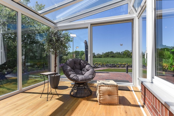 A sunlit room with a glass ceiling, a cushioned chair, a small table, and a potted plant.