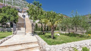 Una escalera de piedra que lleva a un edificio con una puerta de metal, rodeado de follaje y un muro de piedra.