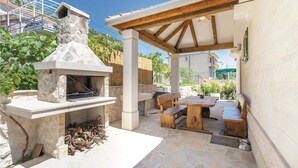 Cocina exterior de piedra con chimenea, bancos de madera y una mesa.
