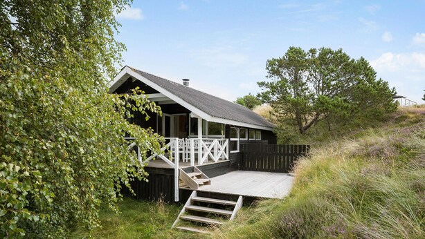 A wooden cabin with a porch and steps leading up to it, surrounded by greenery. - 2 bedroom nice home in Fanø (Fanø)