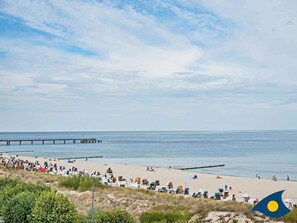 A beach with a pier extending into the water, surrounded by beach chairs and umbrellas.