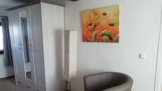 A room with a grey chair, a painting of flowers, and a white wall. - Holiday Bag WE1468 - Holiday Home (Sassnitz)