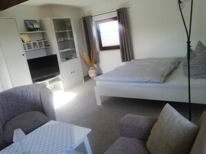 Ein gemütlicher Raum mit Bett, Sofa, Fernseher und kleinem Tisch.