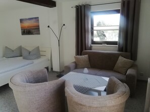 Ein Wohnzimmer mit einer Couch, zwei Sesseln, einem Couchtisch, einer Stehlampe und einem Bild an der Wand.