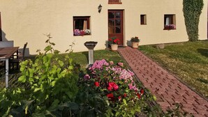 A building with a beige exterior, a red door, and a small garden with flowers and a pathway leading to the entrance. - Holiday Bag WE1468 - Holiday Home (Sassnitz)