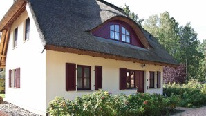A traditional house with a thatched roof, white walls, and red shutters.