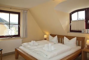 A hotel room with a large bed, two bedside tables, a window with curtains, a radiator, and a wooden bench. - FH Frieda only a few minutes walk to the beach quiet location - FH Frieda only a few minutes walk to the beach (Glowe)