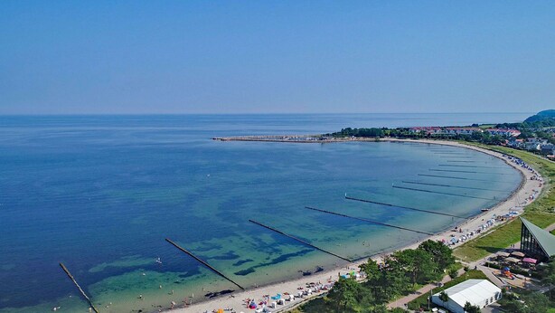 An aerial view of a coastal area with a beach, clear water, and a pier extending into the sea.