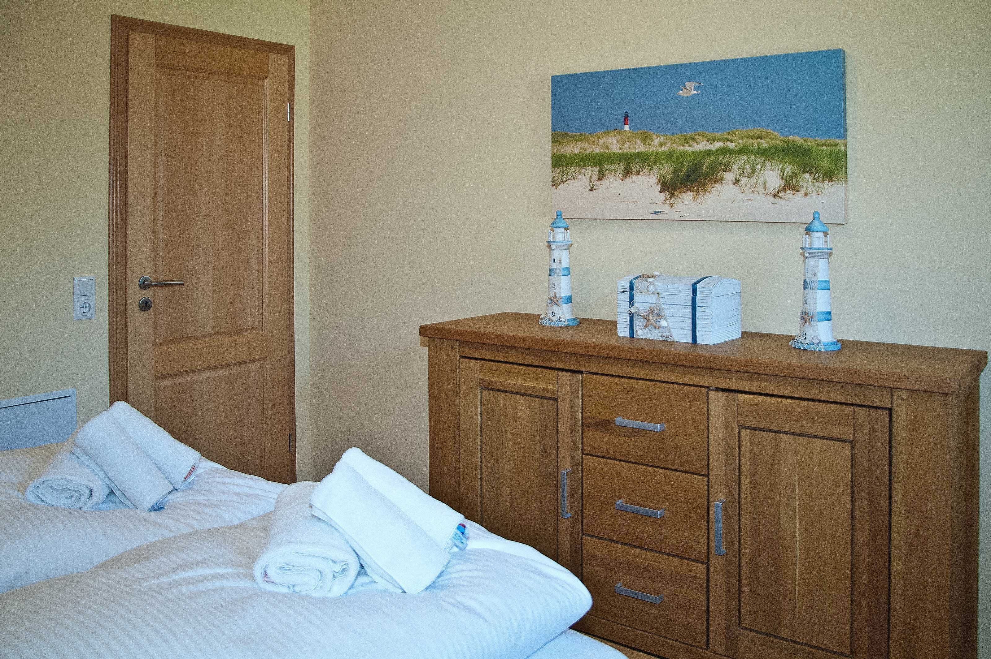 Une chambre d’hôtel avec deux lits, une commode en bois, un tableau représentant un phare et une petite maquette de phare.
