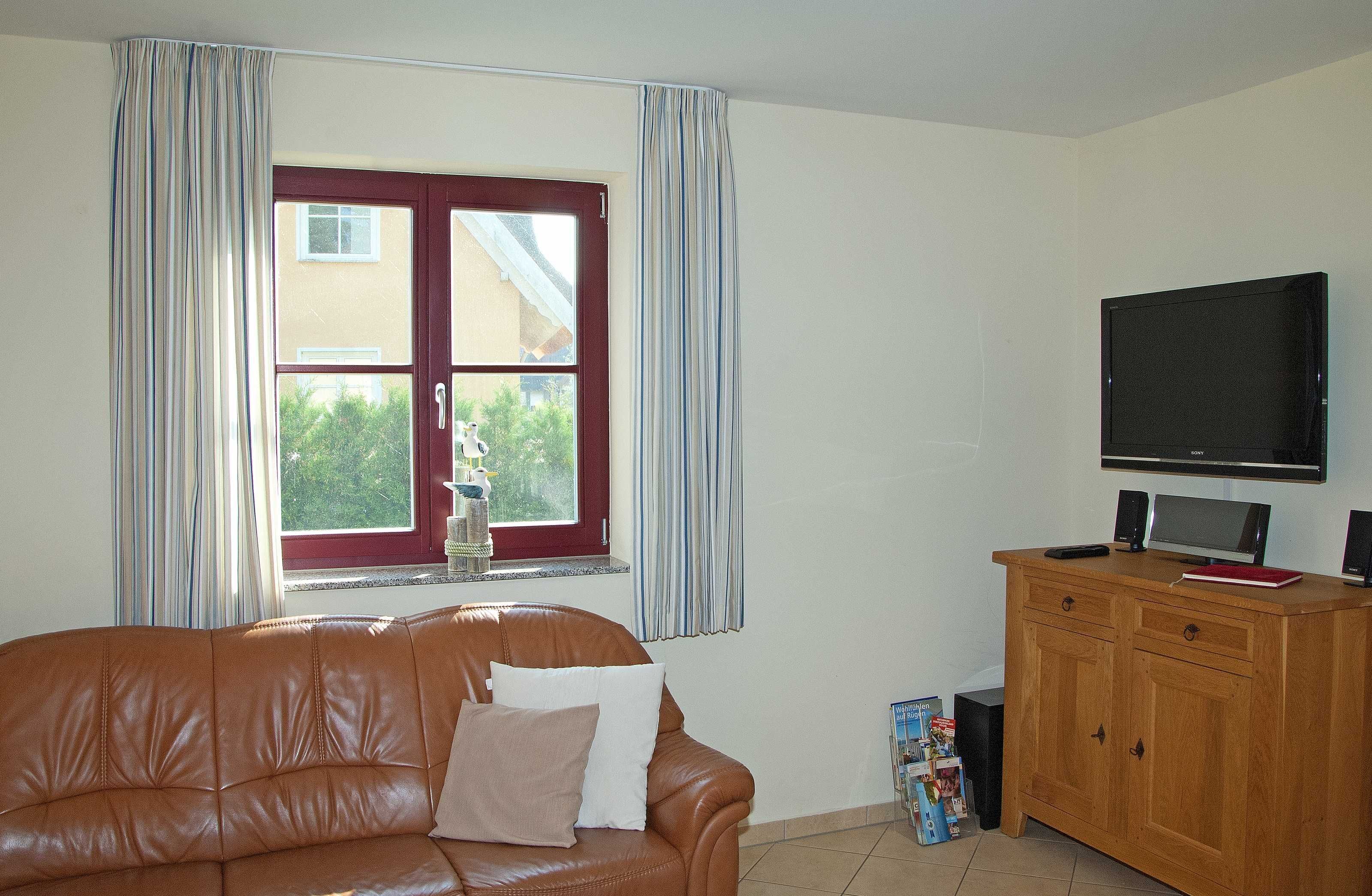 Una sala de estar con un sofá de cuero marrón, un mueble de madera con televisor y una ventana con cortinas.