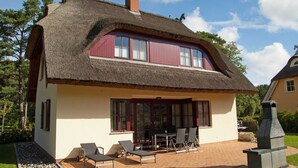 A house with a thatched roof, large windows, and a patio with outdoor furniture.