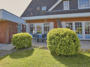 A house with a brick exterior, a tiled roof, and a patio with a table and chairs. - 005 - Hooge (BC.n3) - BUE - Apartment house Seewind (Büsum)